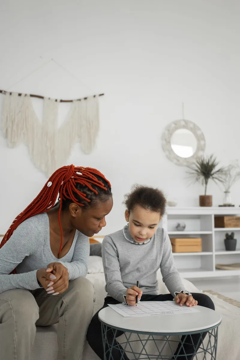 Une mère et sa fille penchées ensemble sur un cahier de devoirs dans un salon