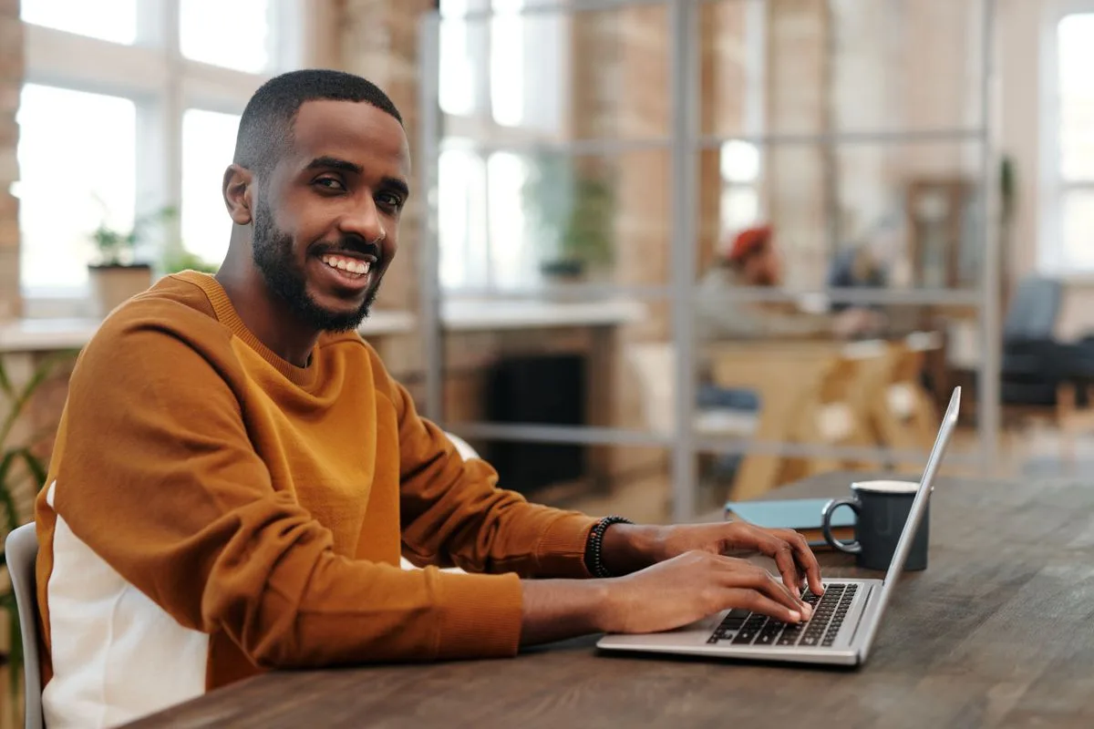 Un homme souriant tape sur un ordinateur portable dans un espace de travail lumineux