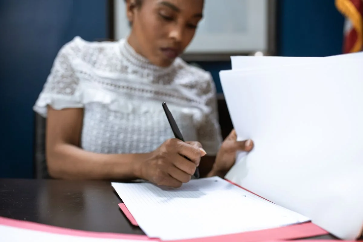 Une femme signe et classe des documents administratifs sur un bureau