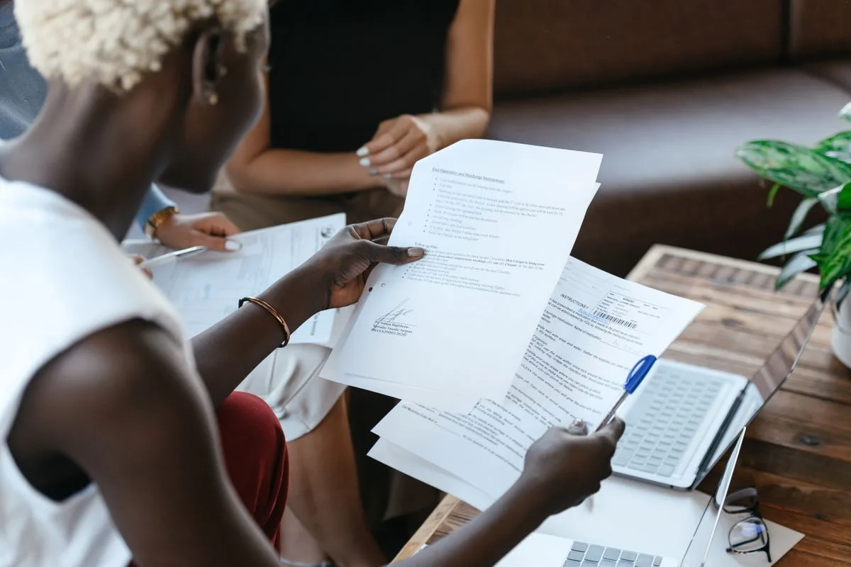 Deux personnes comparent des documents administratifs autour d'un ordinateur portable
